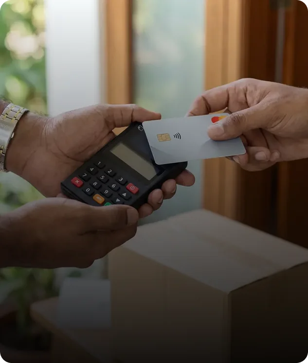 One hand holding a Payable mPOS keypad over a parcel while another taps a contactless card against it.