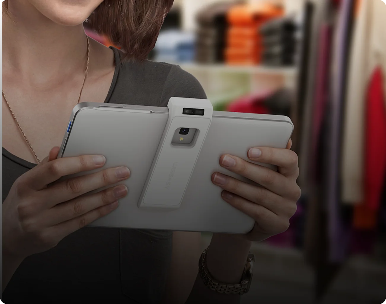 A shop assistant holding a tablet point of sale with a barcode scanner clipped to its back, on the shop floor.